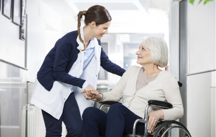 A female caregiver talking to a senior woman in a wheelchair, in a long term care facility