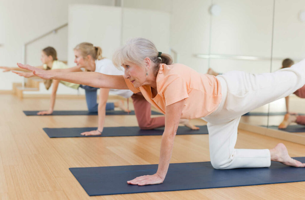 A group of young and old women are exercising and stretching workouts during a yoga class in a fitness studio.