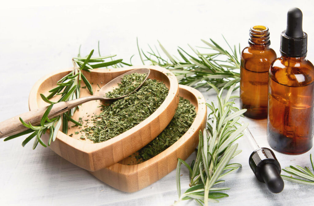 Ground rosemary on a heart-shaped shallow bowl beside two small bottles of essential oil