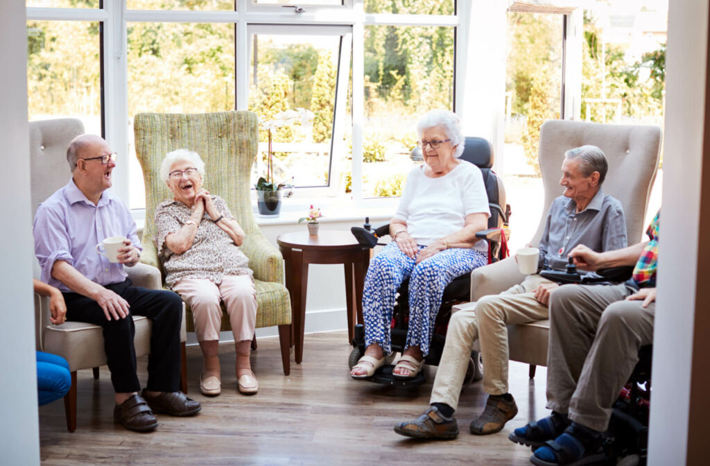 A group of seniors sitting talking to each other and having a cup of tea in a senior living facility.
