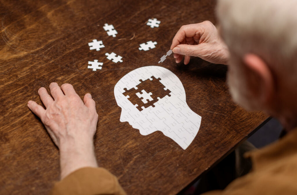a man puts together a puzzle in the shape of a human head, with pieces missing towards the top to represent dementia
