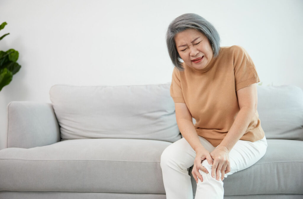 A senior woman suffering from a knee pain while seated on a couch.